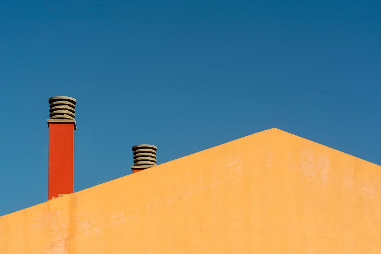 services-01 Minimalist photo of a building facade with chimneys against a clear blue sky.