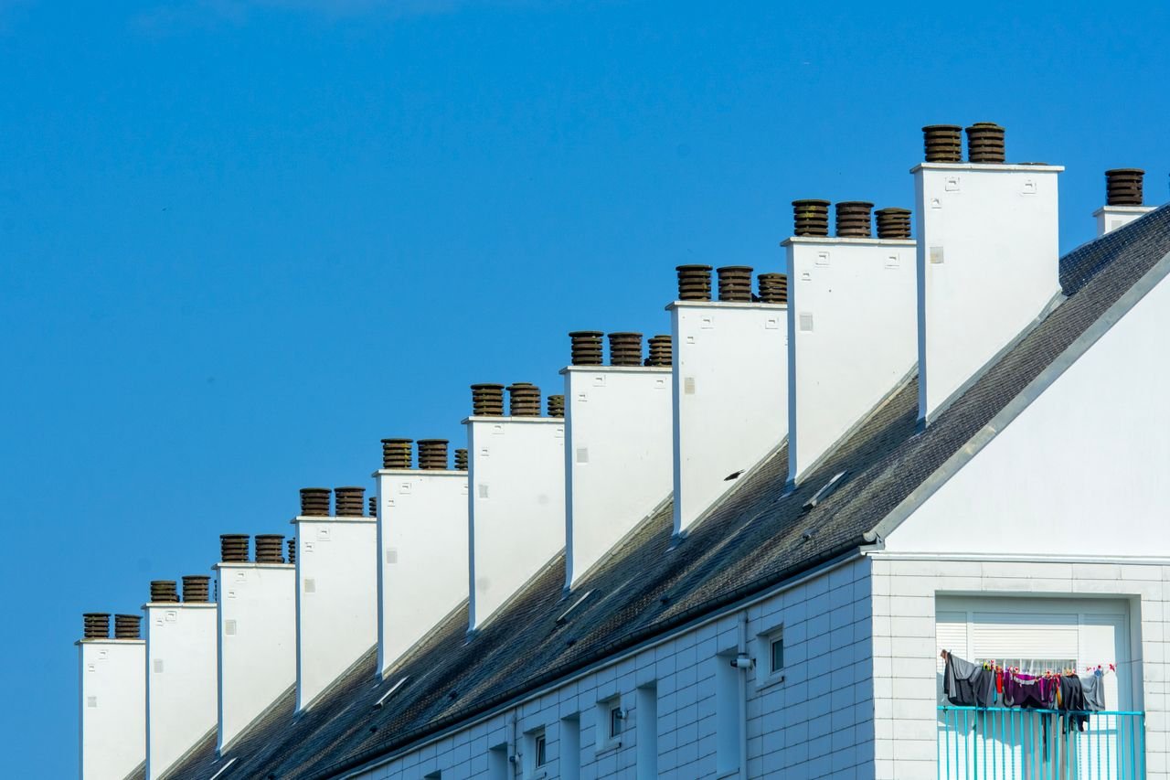 our-value Row of chimneys on modern residential buildings under a clear blue sky. Urban architecture with rooftops.